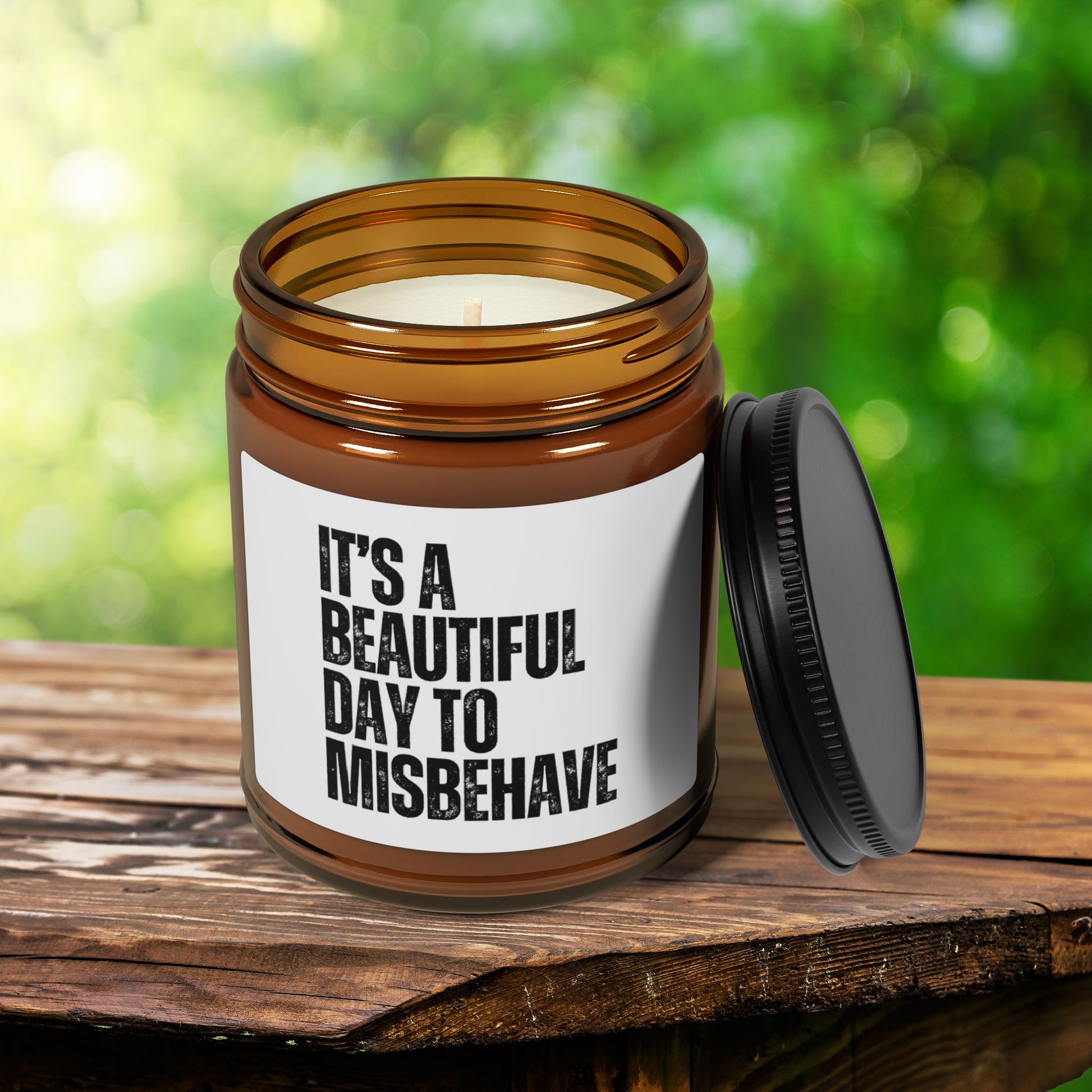 It's a Beautiful Day to Misbehave scented candle in a brown jar on a wooden surface outdoors.