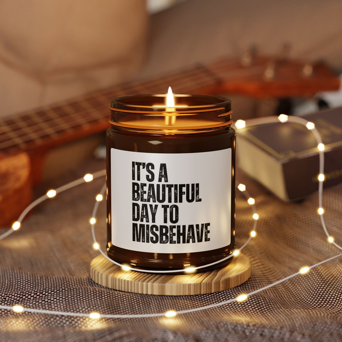 It's a Beautiful Day to Misbehave scented candle, surrounded by string lights and a guitar in the background