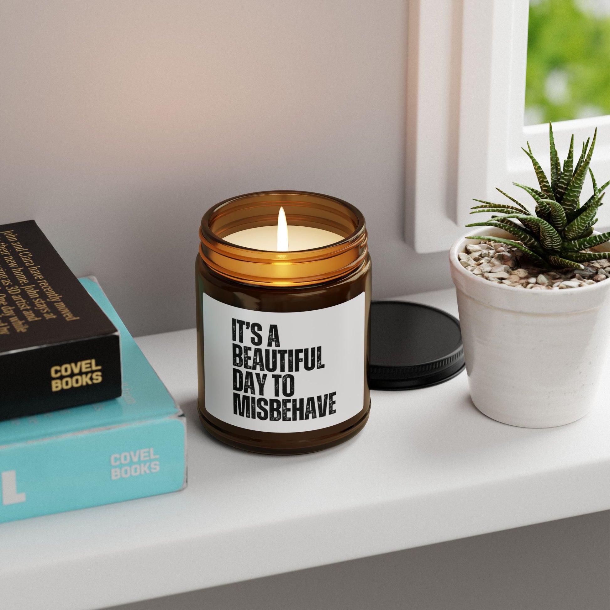It's a Beautiful Day to Misbehave scented candle on a shelf next to books and a plant