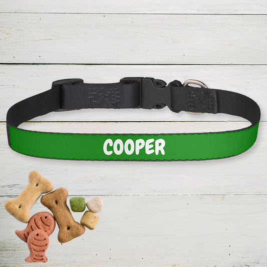 Green dog collar personalized with 'COOPER' printed on it, placed on a wooden surface with dog treats.